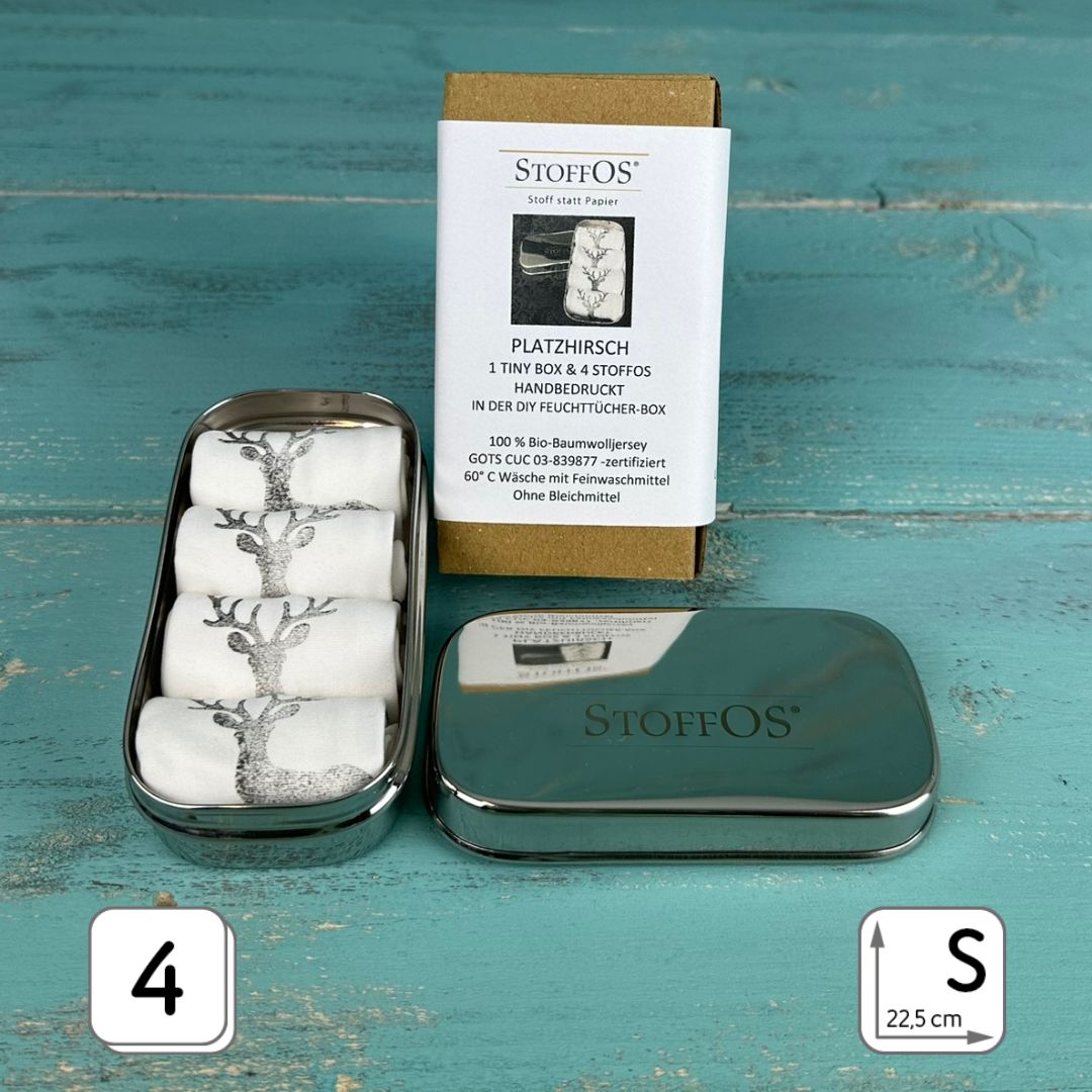 Edelstahlbox geöffnet, 12,5 x 6,5 x 4 cm groß, darin liegen vier aufgerollte StoffOS in Weiß mit dunkelgrauem Aufdruck Motiv Platzhirsch. rechts davon liegt der Deckel mit dem Firmenloge STOFFOS graviert. Dahinter steht der Geschenkkarton mit einer bedruckten Banderole.