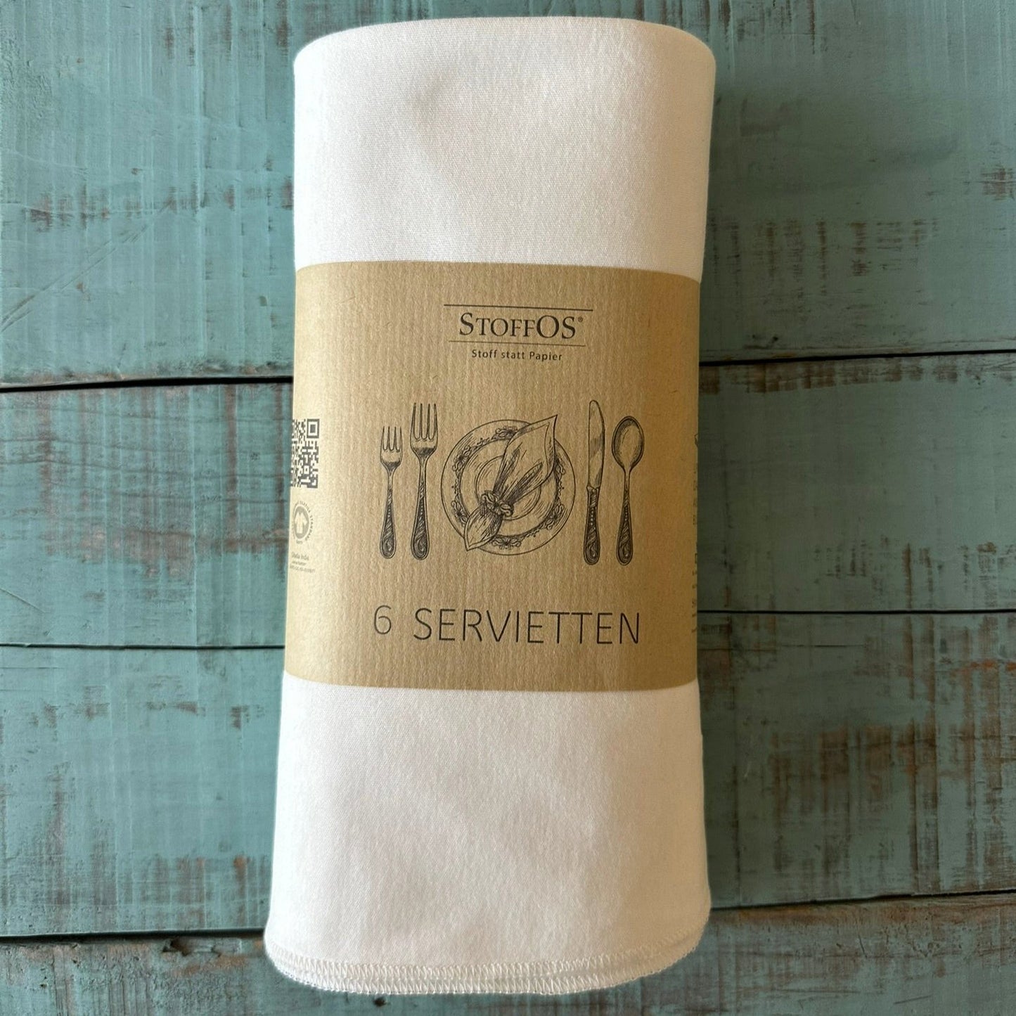 Die sechs naturweissen Stoffservietten sind aus Biobaumwoll-Interlockjersey. Eine braune Banderole ist mit einem historischen Stich eines Gedecks bedruckt. Die Banderole ist um das Bündel gewickelt.