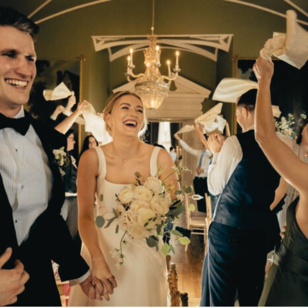 Eine neue Sitte ist es bei Hochzeiten mit Servietten über den Köpfen zu schwenken, wie hier wird ein Hochzeitspaar von Spalierstehenden in festlicher Kleidung so gefeiert.