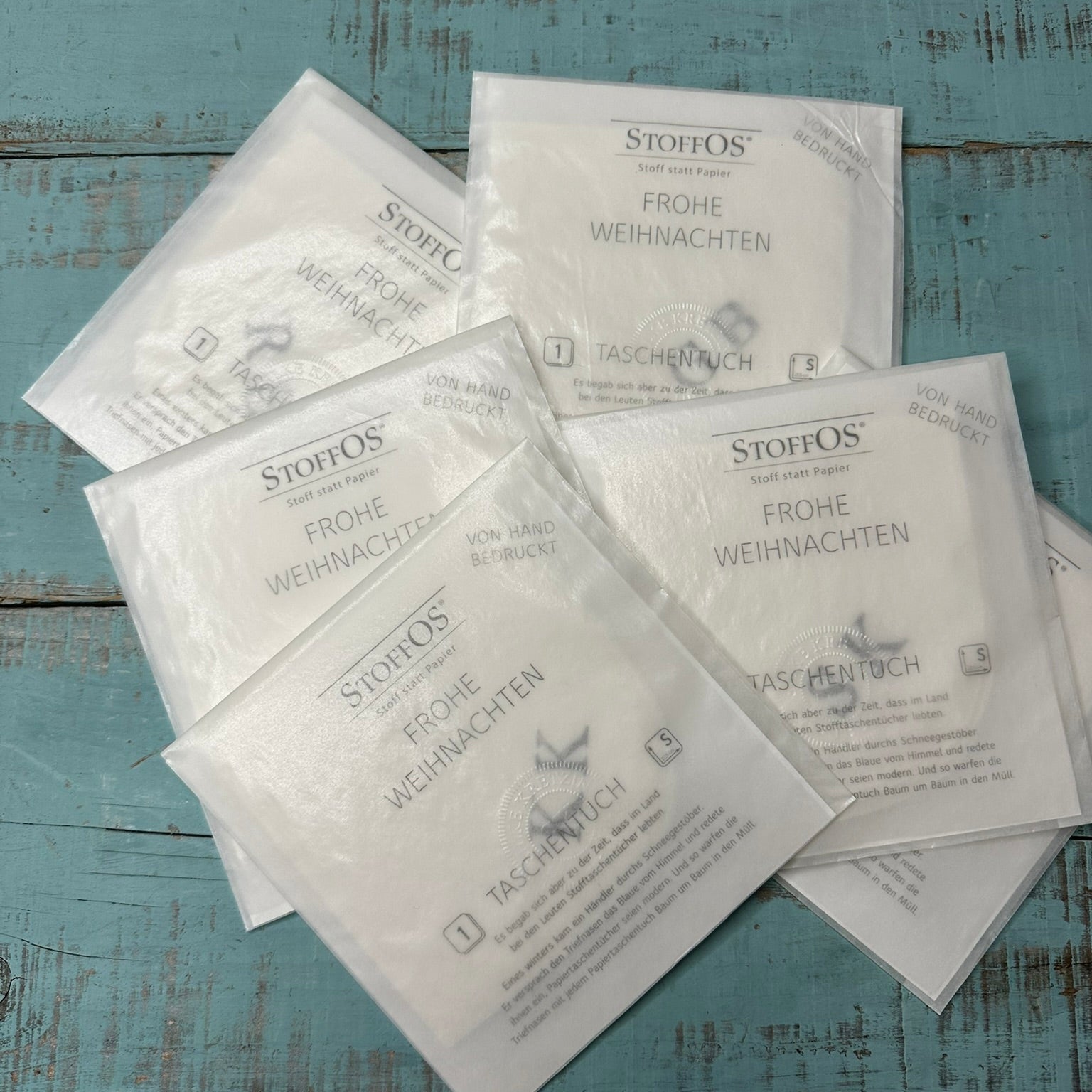 Musterbilder für personalisierte Stofftaschentücher, einzeln von HAnd bedruckt mit Musterinitialen. In Pergamintüten verpackt, Weihnachtsgruß auf der Verpackung. Außeralb der Saison erfolgt Verpackng ohne Weihnachtsgruß.