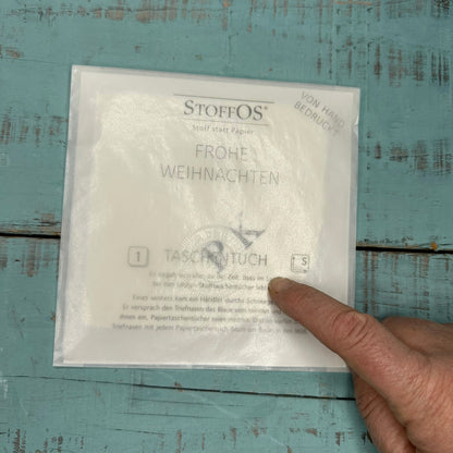 Ein einzelnes weißes Stofftaschentuch Gr. S 22,5 x 22,5 cm in Pergamintüte verpackt, mit Frohe Weihnachten außerhalb der Saison neutral ohne Weihnachtsgruß verpackt.