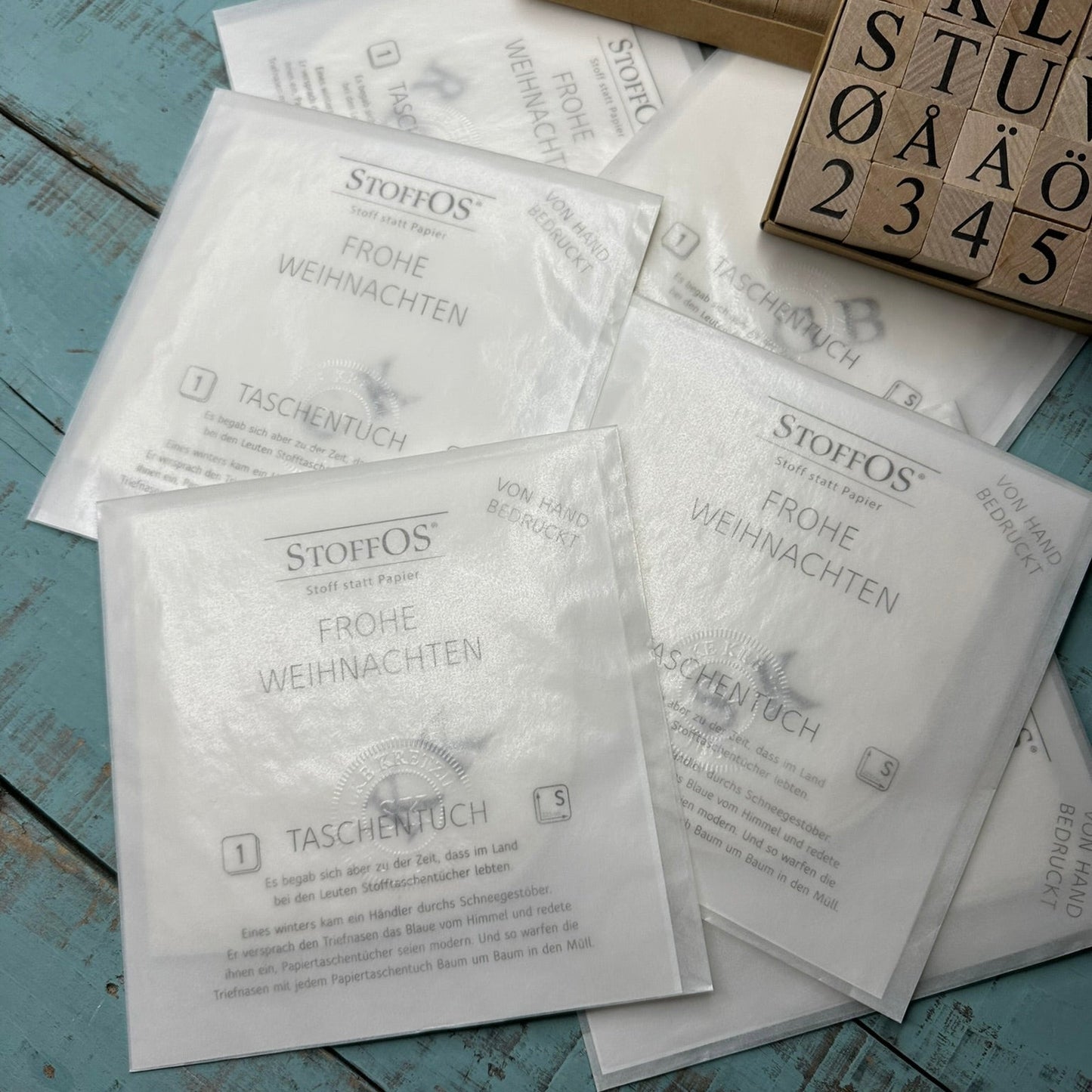 Einzelne weiße Stofftaschentücher Größe S, 22,5 x 22,5 cm, mit Initialen von Hand bedruckt, durch die Pergamintüte sichtbar, saisonal mit Frohe Weihnachten verpackt, außerhalb der Weihnachtssaison erfolgt die Verpackung neutral, ohne Weihnachtsgruß.