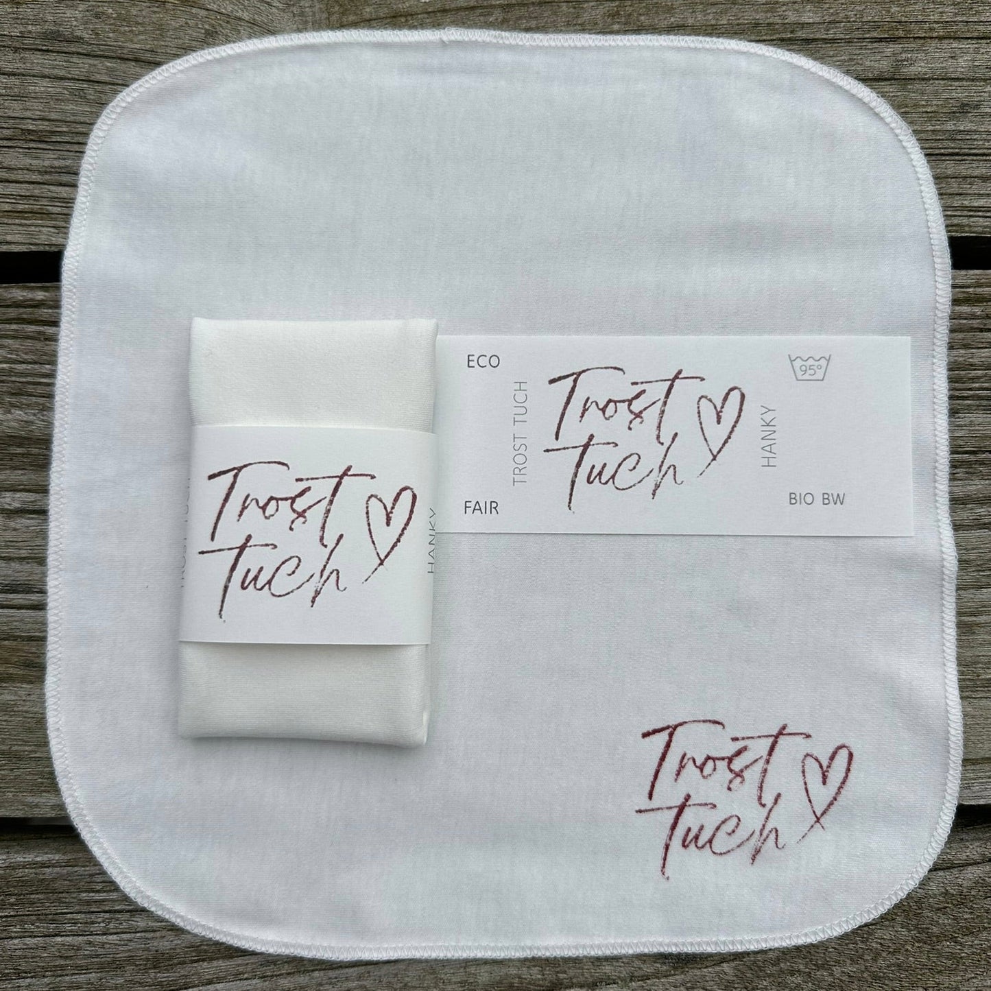 eine Tuch flach liegend in Gr. S 22,5 x 22,5 cm mit BAnderole, auf der Pflegeanweisungen, Trosttuch und Hanky aufgedruckt sind, ein StoffO gefaltet, hochformat, mit Papierbanderole umwickelt, mit dem Tuchdruck-Motiv bedruckt.